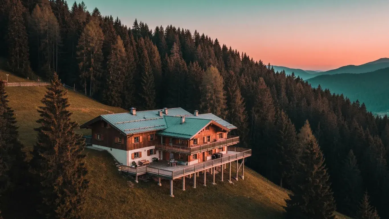 An sweeping aerial photograph of a mountain chalet perched above the treeline, at dusk