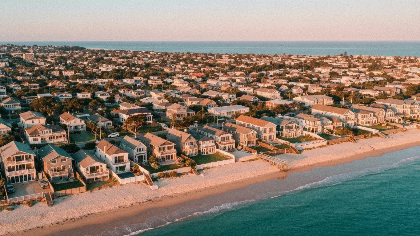 An sweeping aerial photograph of a cluster of beach houses along a shoreline, at golden hour