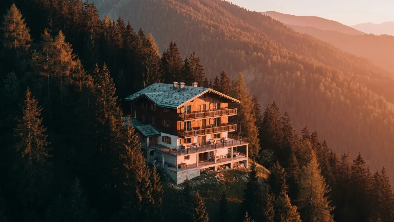 An aerial drone photograph of a mountain chalet perched above the treeline, at golden hour