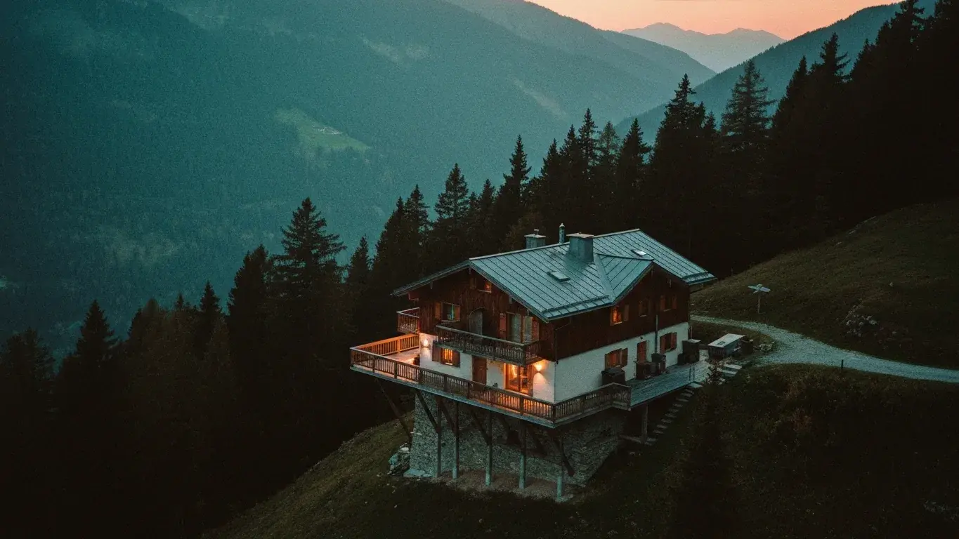 An high overhead photograph of a mountain chalet perched above the treeline, at dusk