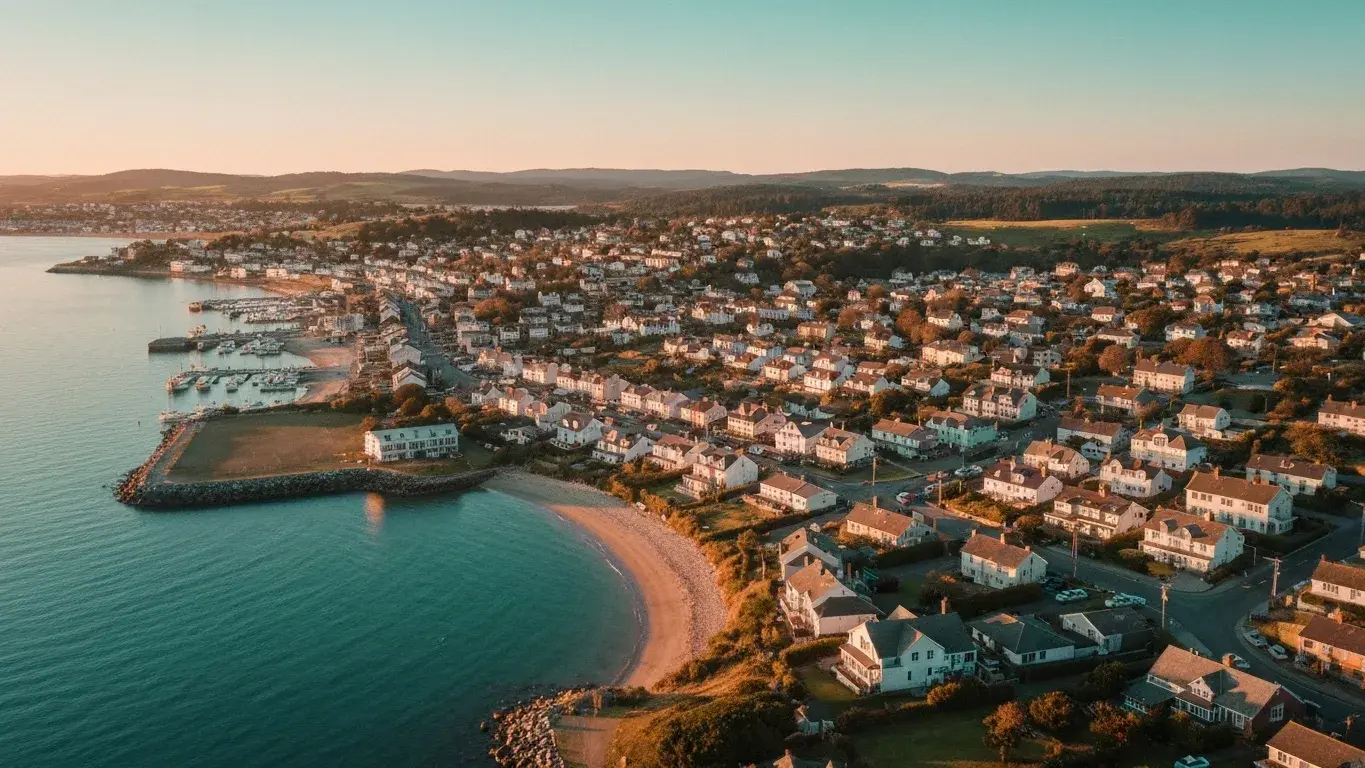 An sweeping aerial photograph of a small coastal town hugging the water, at golden hour
