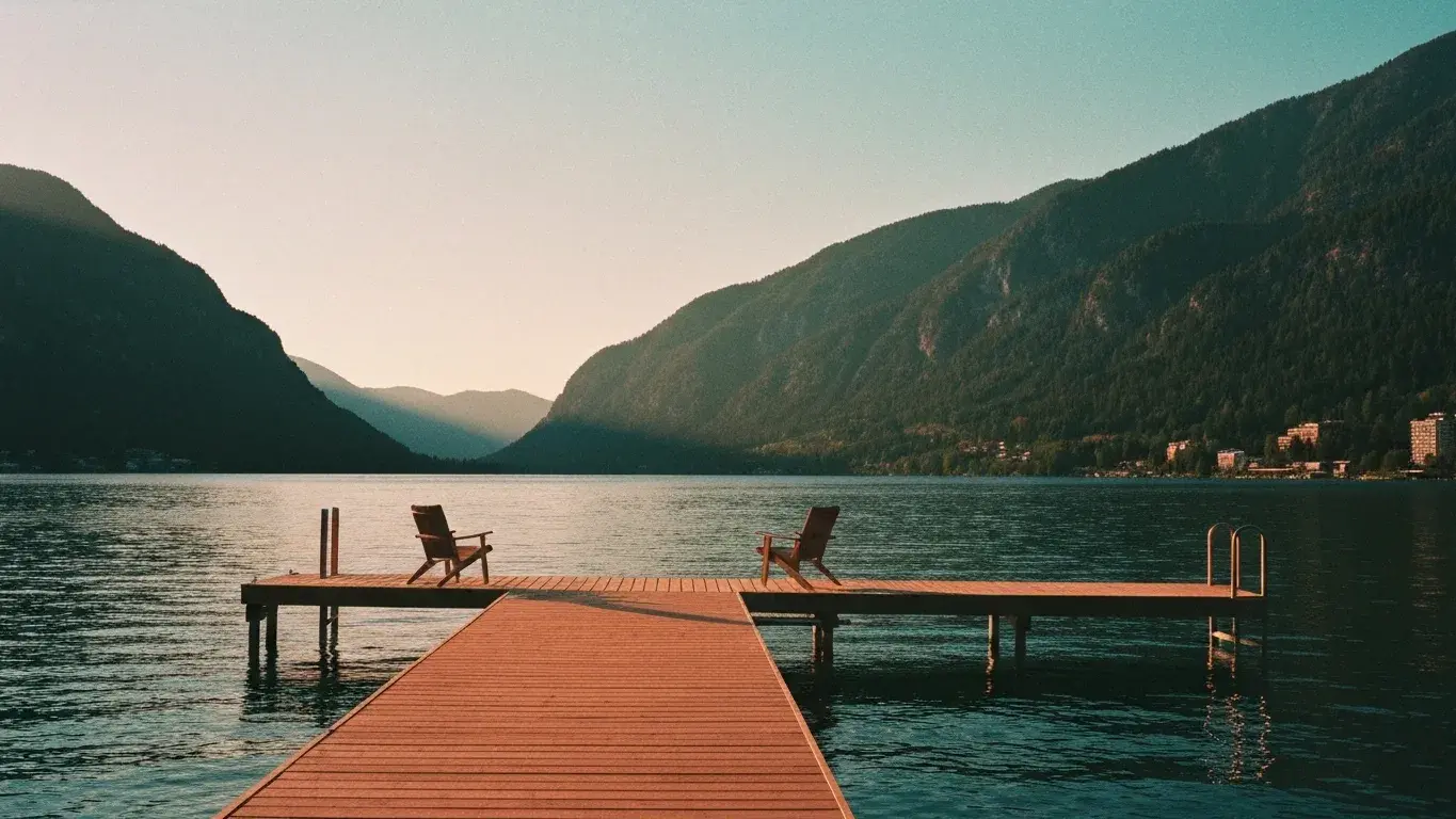 atmospheric wide photograph of a private lakeside dock with chairs overlooking a mountain valley, at golden hour