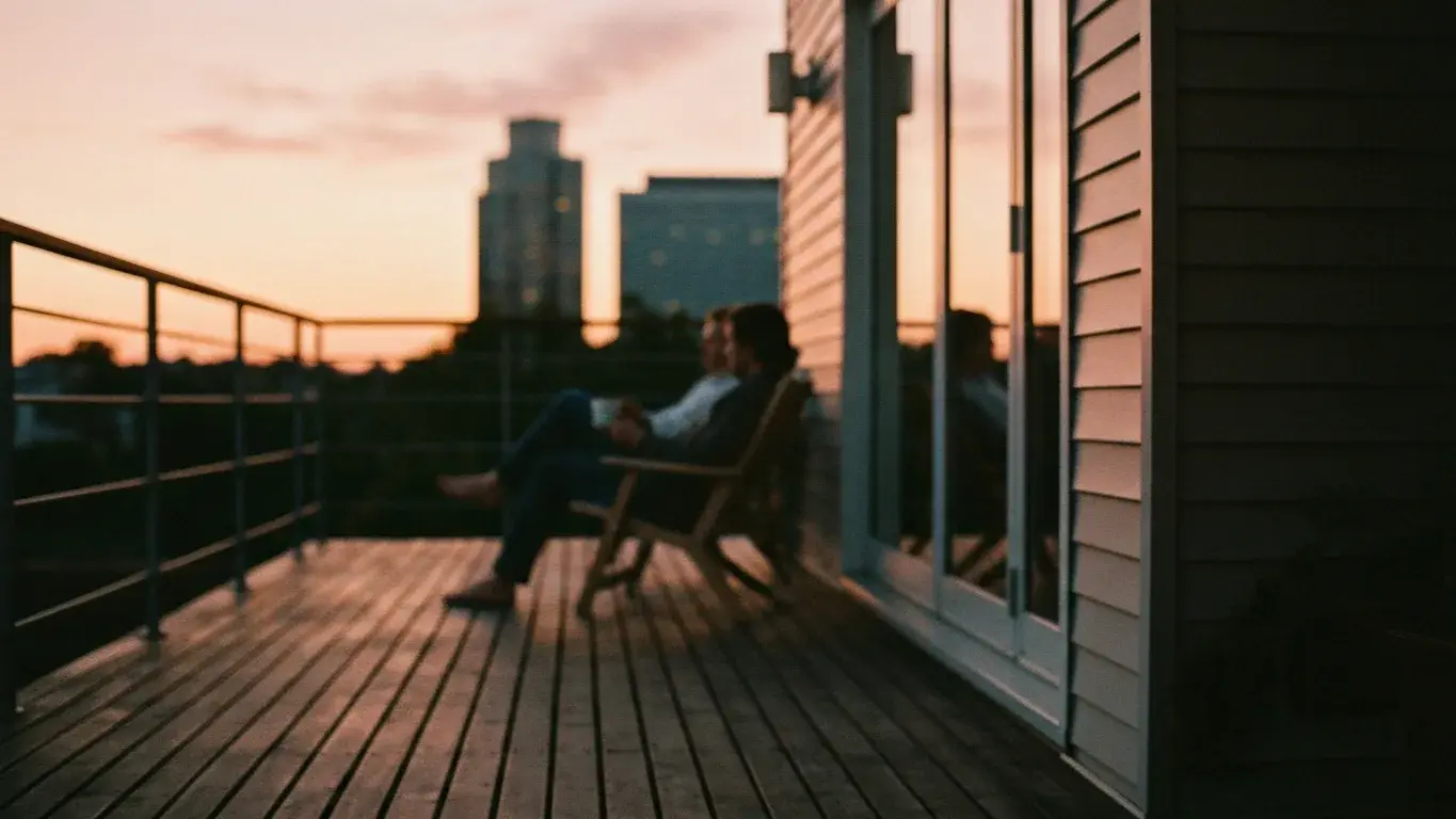 intimate detail photograph of two distant figures relaxing on a deck with coffee, at warm dusk