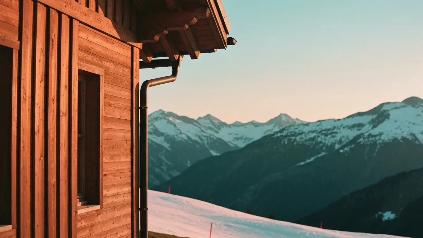 intimate exterior detail photograph of a mountain ski chalet set in snowy alpine slopes, warm sunset, lush summer