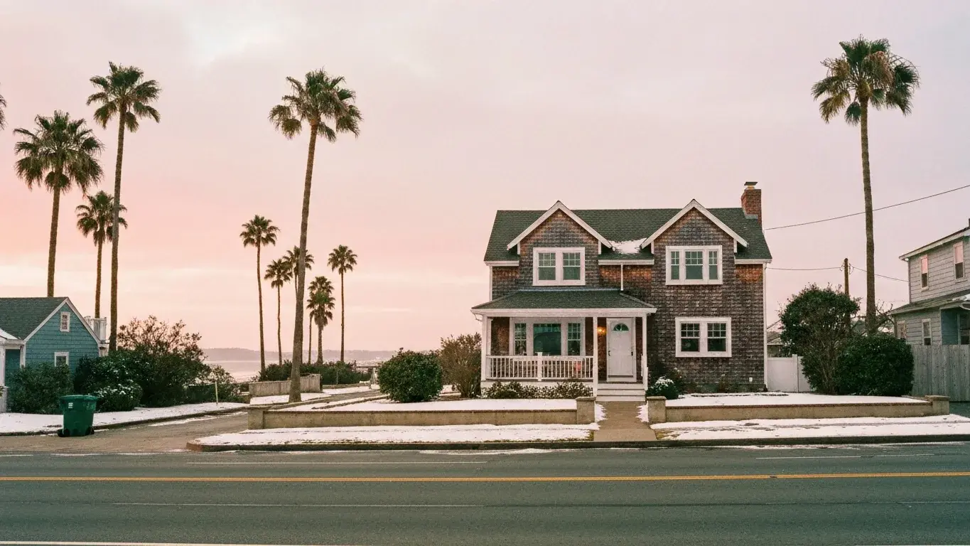 wide establishing exterior photograph of a cape cod cottage set in a palm-lined coastal street, a soft overcast afternoon, fresh winter snow