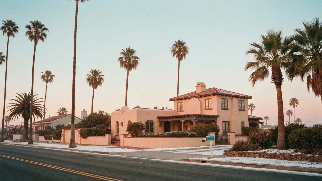 wide establishing exterior photograph of a Spanish-style casita set in a palm-lined coastal street, early misty dawn, fresh winter snow