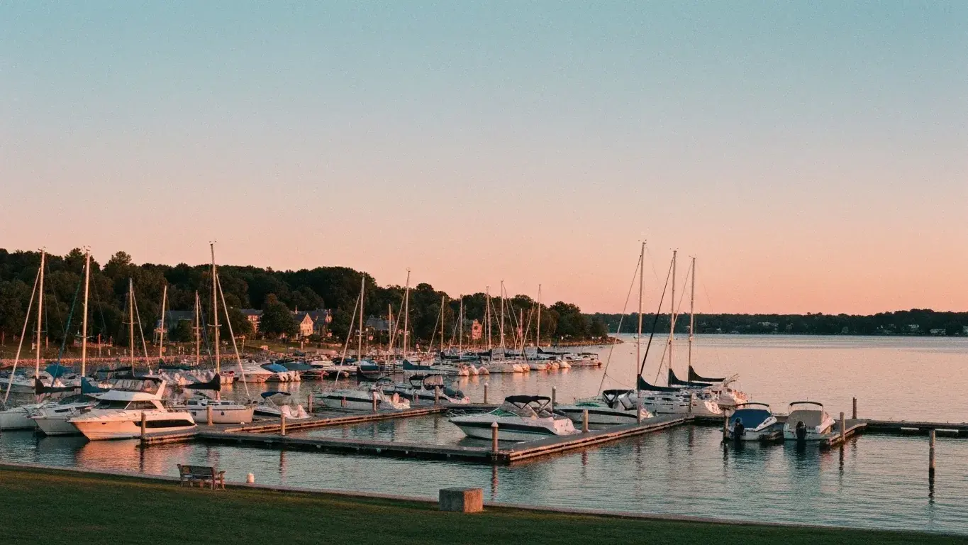 wide documentary photograph of a lakeside marina dotted with boats, at warm dusk