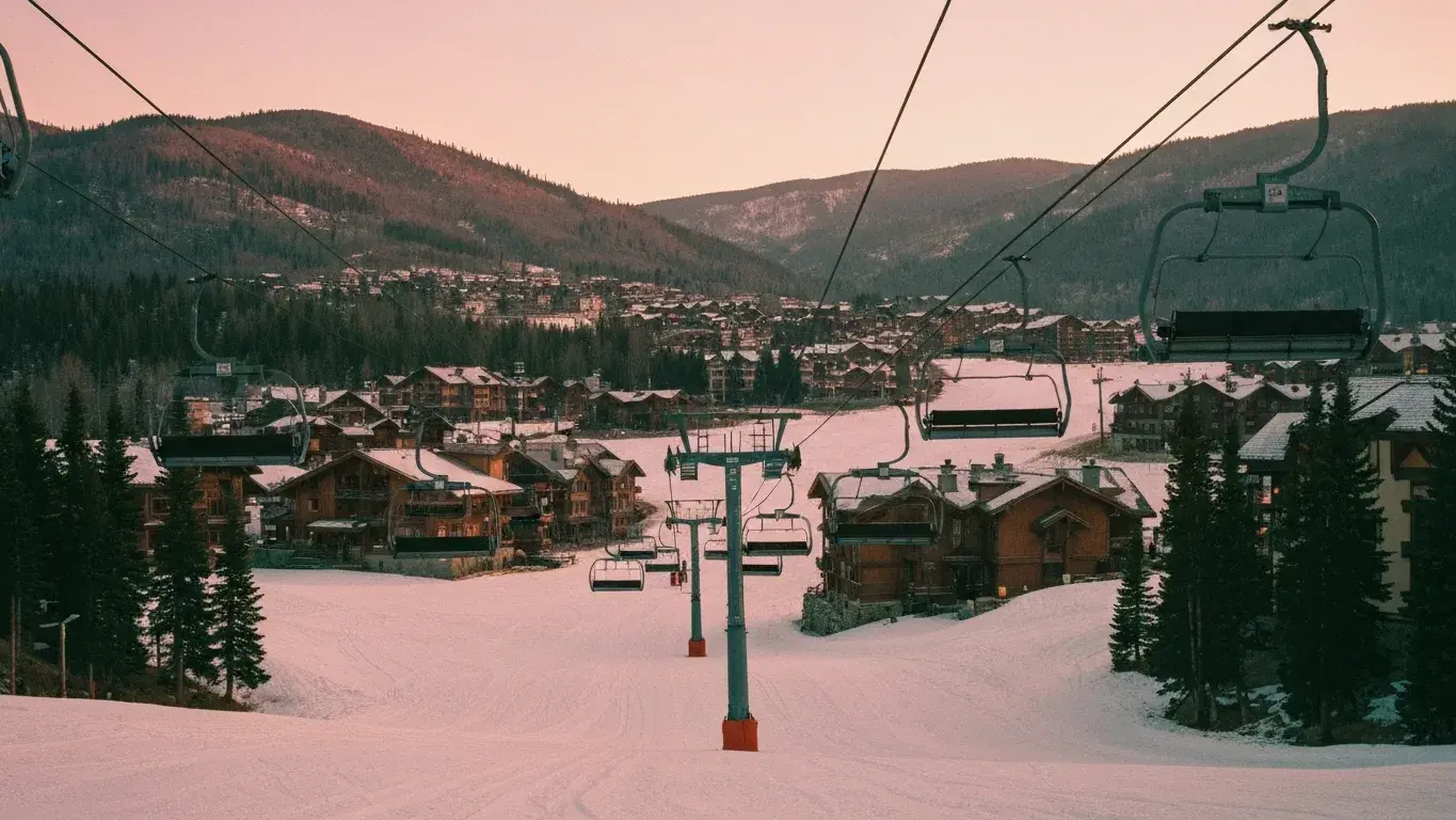 wide documentary photograph of a mountain town with ski lifts, at warm dusk